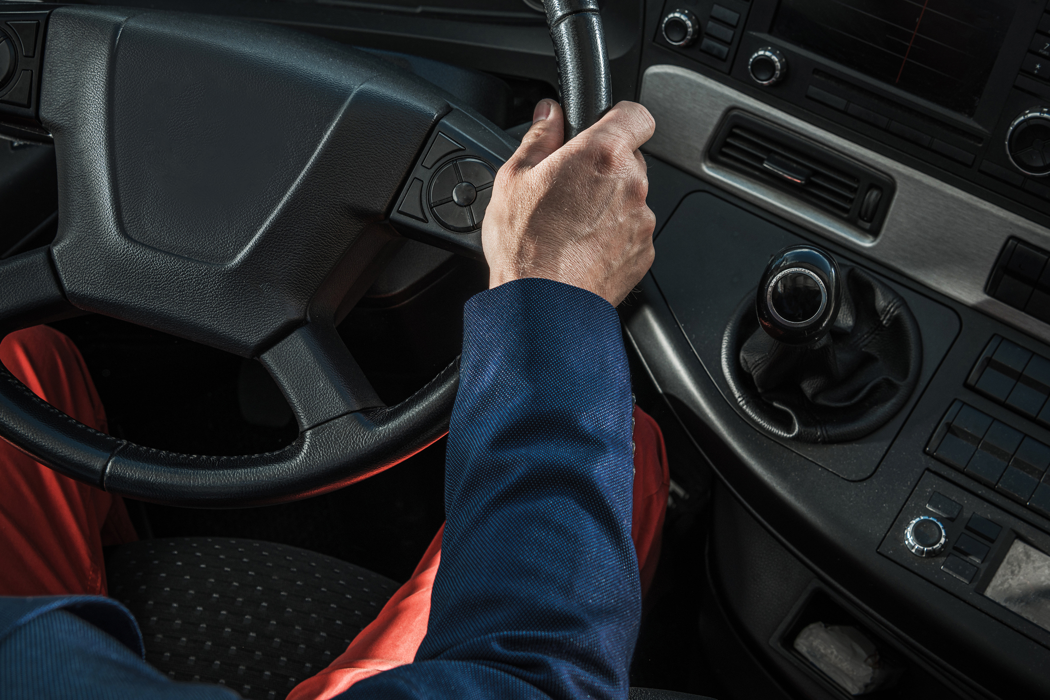 Close-up view of a truck driver's hand on the steering wheel inside the cab.